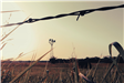 An image of an old windmill as seen through a barbed wire fence. 