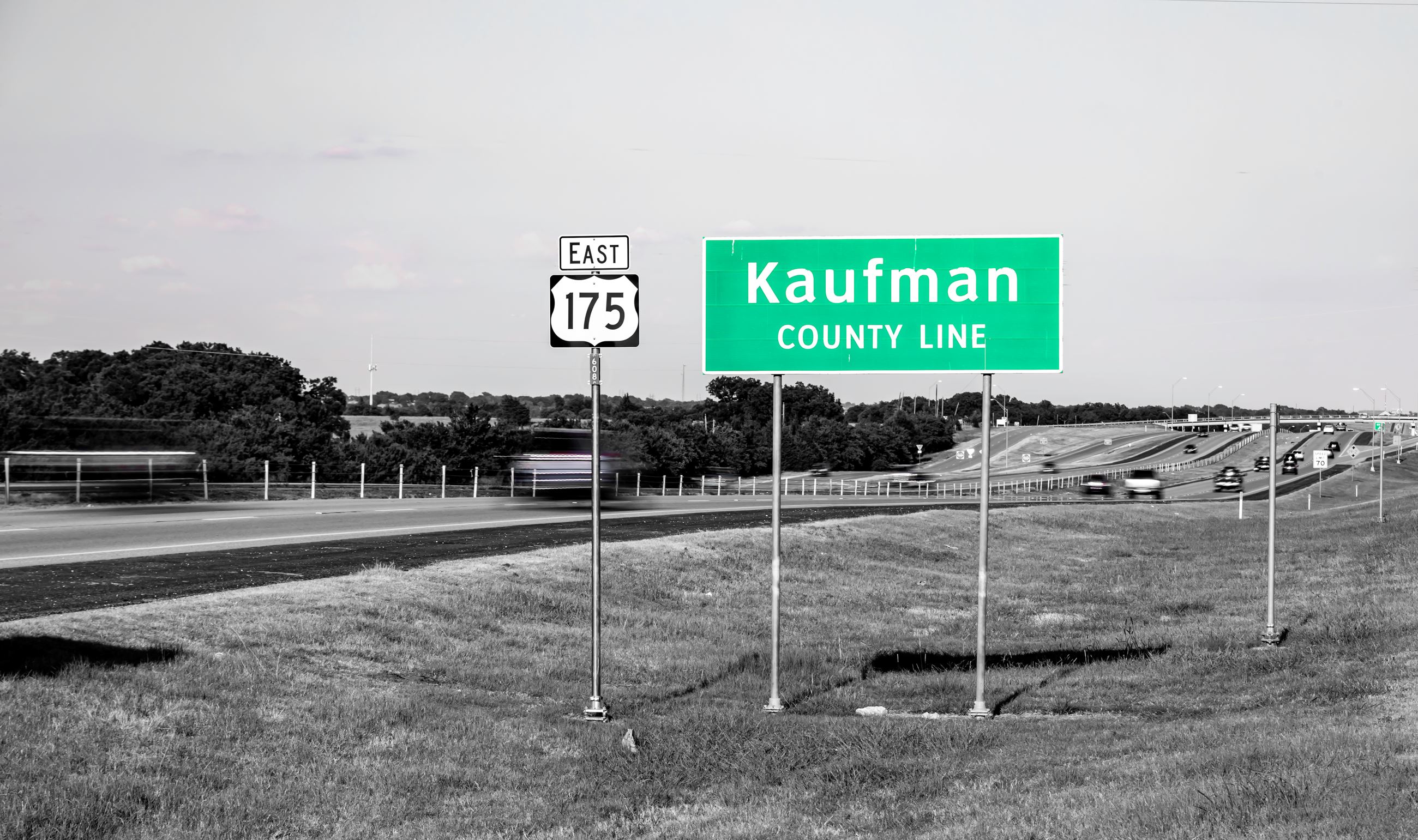 A black and white image of the green and white Kaufman County Line sign on east US 175.. 