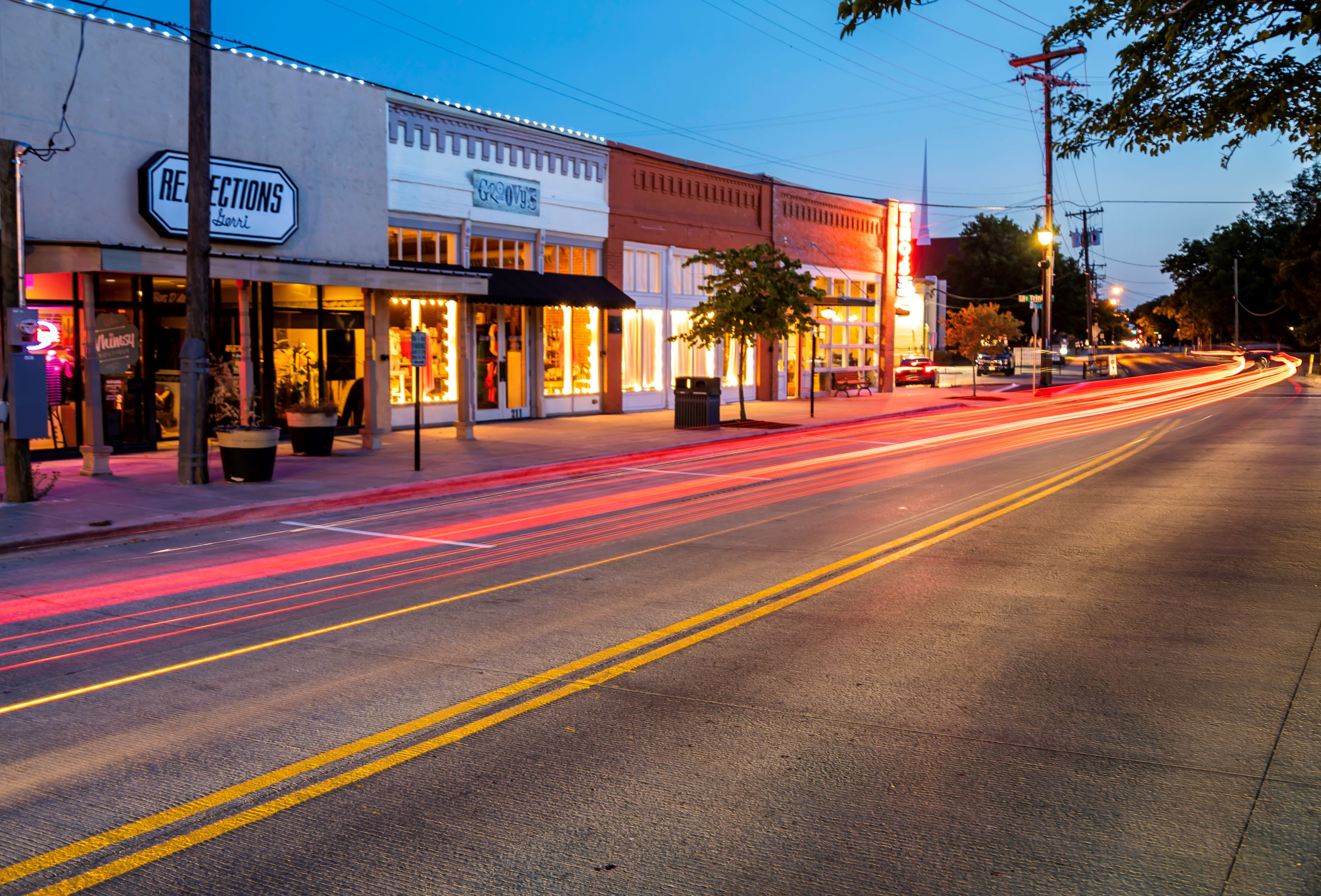 An image of timelapse car tail lights whisking by the shops in old downtown Forney.